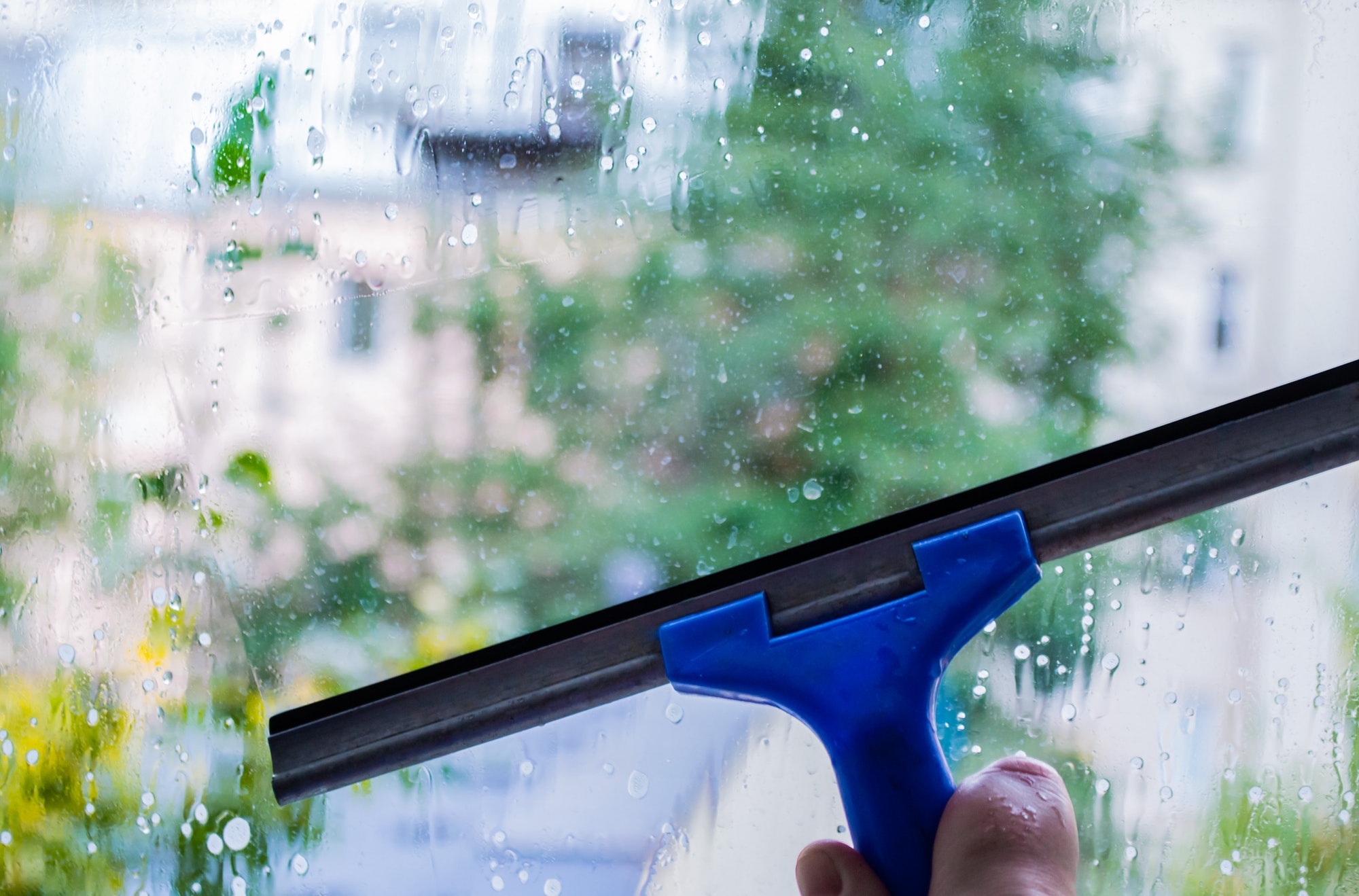 Window pane cleaning, housework with special squeegee. Outside the window blurred street